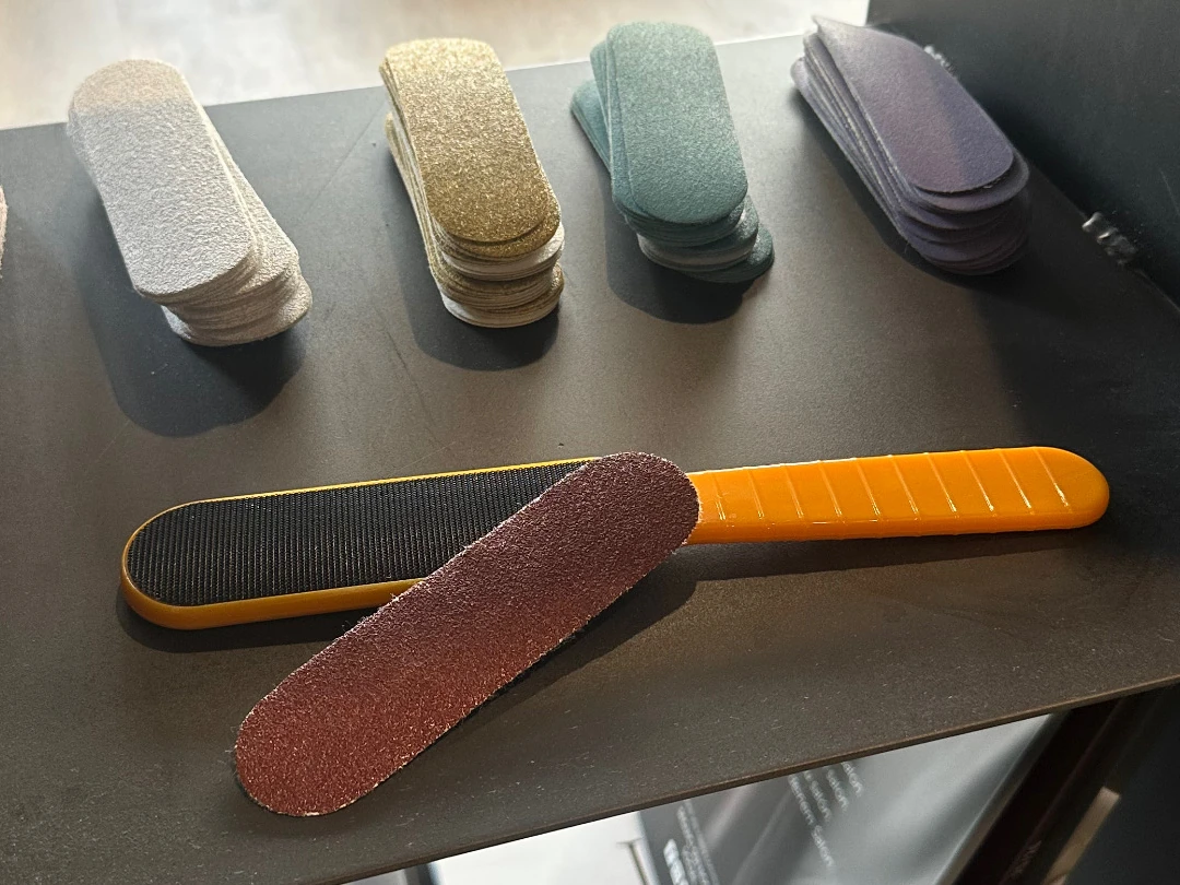 Raspa per pedicure con supporto arancione, abrasivo separato e ricambi di diversi colori esposti su un tavolo