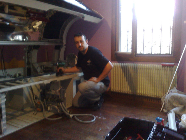 Technician kneeling beside a partially dismantled UWE professional sunbed during technical work in Italy